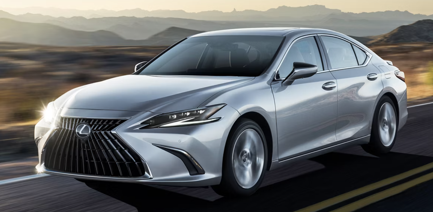 2025 Lexus ES 300H A silver Lexus ES 300H is driving down the highway at sunset.