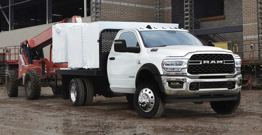 A white Ram Chassis Cab truck is pulling a piece of red equipment.