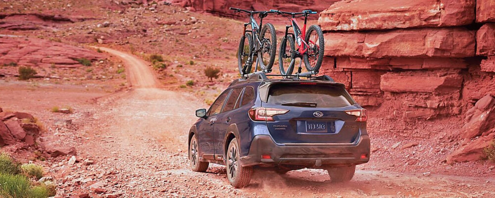 2024 Subaru Outback with bike on roof driving near mountains