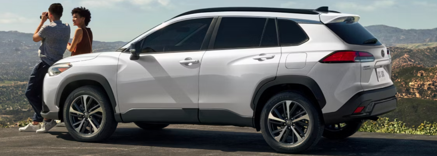 2025 Toyota Corolla Cross Hybrid Two people are standing in front of a white SUV.