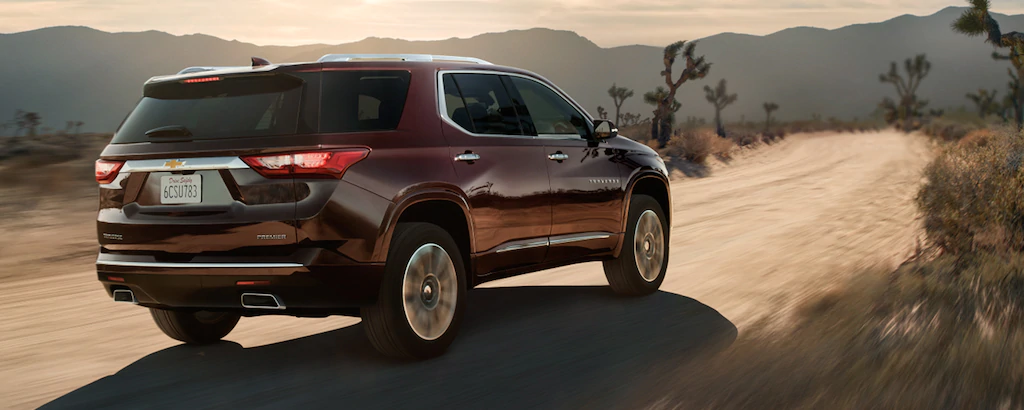2021 Chevy Traverse Rear view of a maroon 2021 Chevy Traverse driving down a dirt path