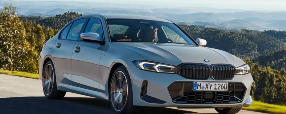 A silver BMW 3. Series is driving on the highway in the hills. 