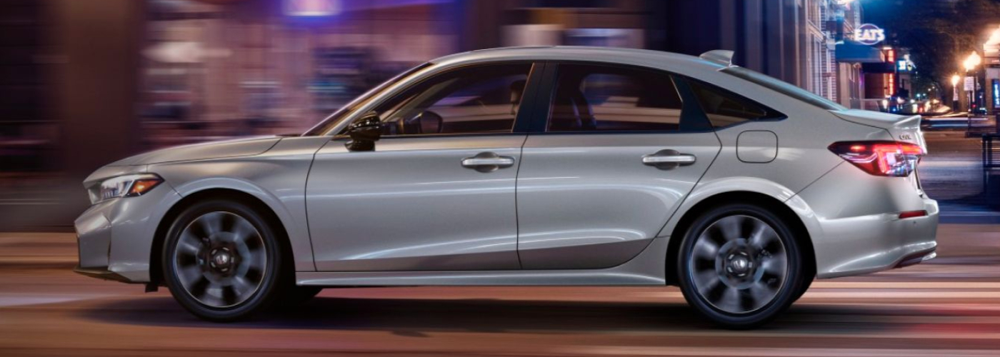 The silver car is driving down a city street at night.