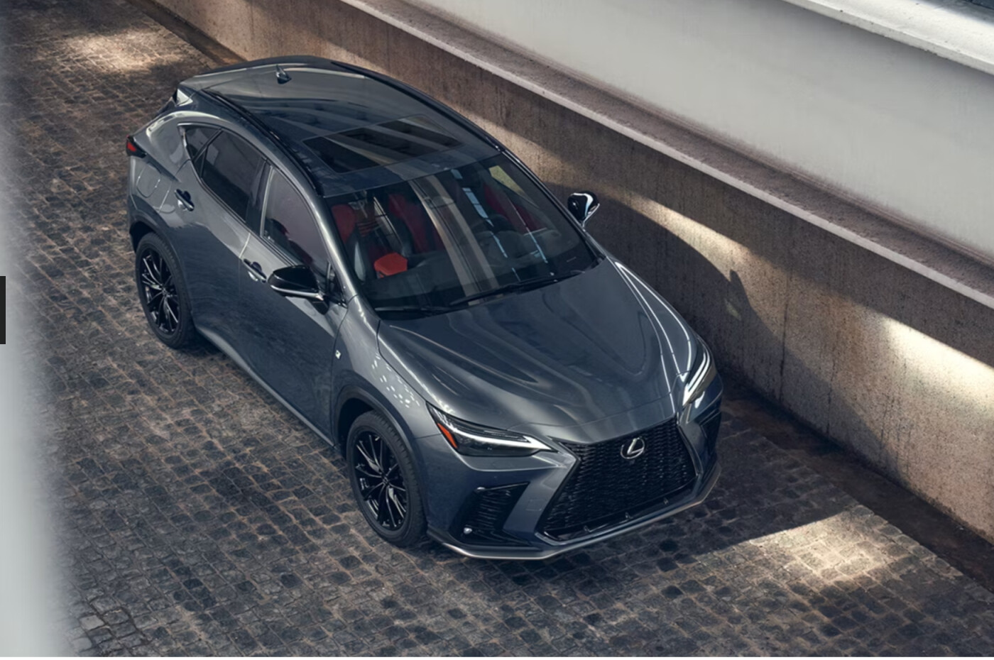 A charcoal gray Lexus NX Hybrid is parked near a cement wall. 