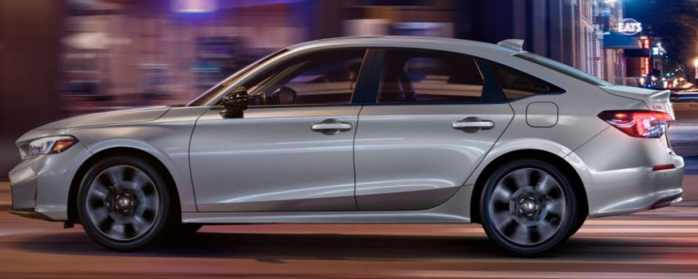 The silver car is driving down a city street at night.