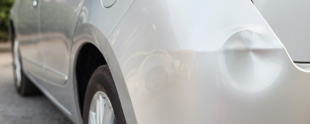 Silver car with a dent on the bumper
