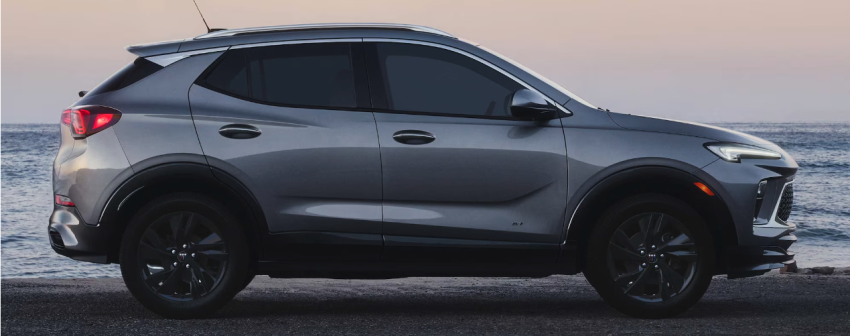 A silver Encore GX SUV is parked on the beach near the ocean. 