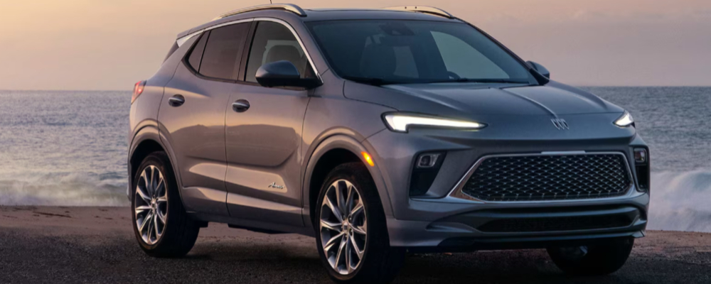 A silver SUV is parked near the ocean at sunset.