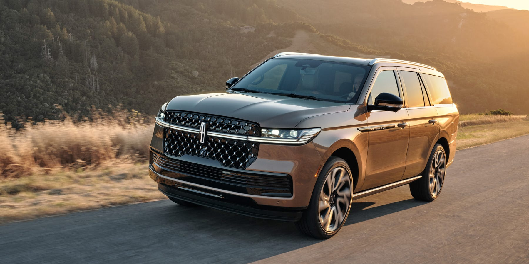 Front three-quarter view of a bronze 2026 Lincoln Navigator SUV driving along a paved road.