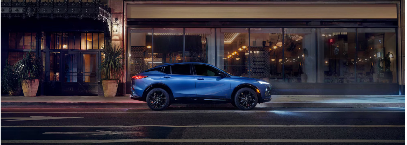 A blue Buick Envista is driving with their headlights on down a city street. 